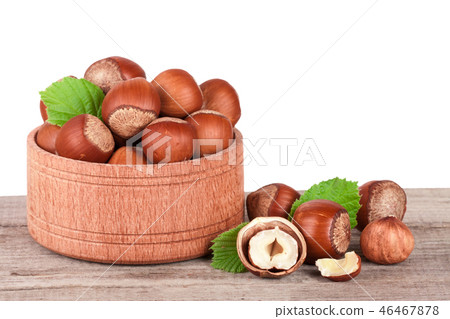 Hazelnuts with leaves in a wooden bowl on a wooden table with a white background Hazelnuts with leaves in a wooden bowl on a wooden table with a white background 46467878
