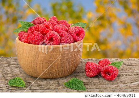 Raspberry in a wooden bowl on table with a blurry garden background Raspberry in a wooden bowl on table with a blurry garden background 46469011