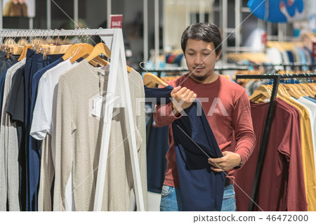 Smart asian man with beard choosing clothes in clothing store at shopping center, looking colorful t-sshirts , Fashion and Consumerism Concept. 46472000