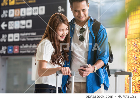Asian couple traveler using the smart mobile phone for check-in at the flight information screen in modern an airport, travel and transportation with technology concept. Asian couple traveler using the smart mobile phone for check-in at the flight information screen in modern an airport, travel and transportation with technology concept. 46472152