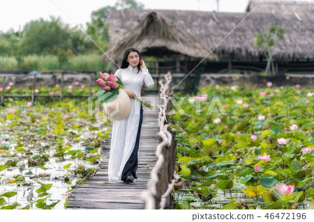 Portrait of beautiful vietnamese woman with traditional vietnam hat holding the pink lotus walking on the wooden bridge in big lotus lake, vietnam, aisan or southeast asia travel concept 46472196