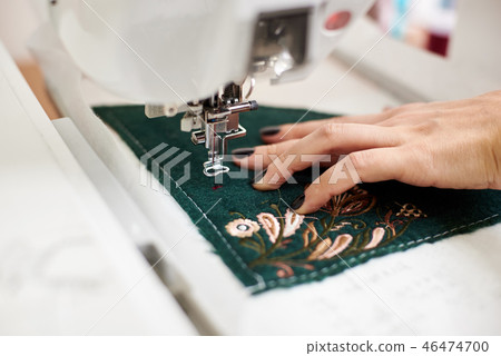 Close-up of woman hand working on sewing machine creating colorful floral pattern on textile detail. Close-up of woman hand working on sewing machine creating colorful floral pattern on textile detail. 46474700