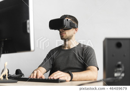 Young man wearing virtual reality goggles headset, vr box and sitting in the office against computer 46489679
