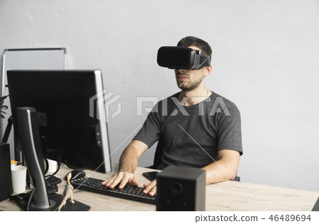 Young man wearing virtual reality goggles headset, vr box and sitting in the office against computer 46489694