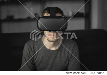 Young bearded man wearing headset of virtual reality in office sitting on a sofa. Young bearded man wearing headset of virtual reality in office sitting on a sofa. 46489854