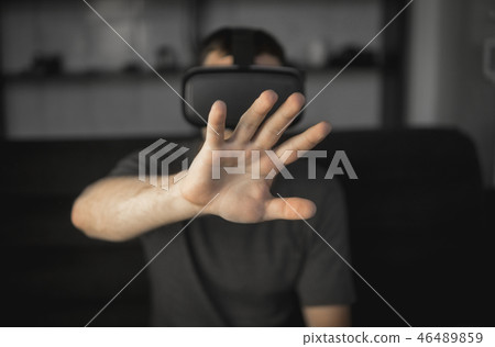 Young bearded man wearing headset of virtual reality in office sitting on a sofa and trying to touch Young bearded man wearing headset of virtual reality in office sitting on a sofa and trying to touch 46489859