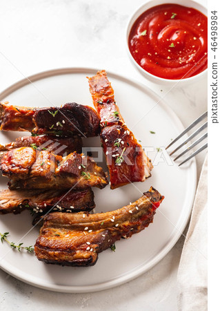 Bbq pork ribs with chili sauce on white plate. Pork ribs on slate background. Copy space. Bbq pork ribs with chili sauce on white plate. Pork ribs on slate background. Copy space. 46498984