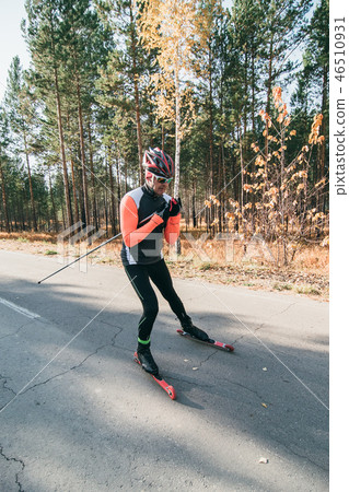Training an athlete on the roller skaters. Biathlon ride on the roller skis with ski poles, in the 46510931