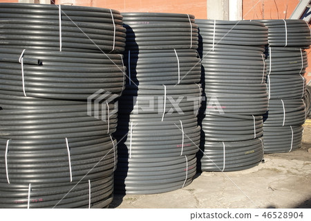 Coiled black plastic pipes stored outdoors 46528904