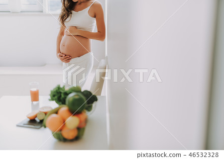 Future mum holding hands on belly and standing in kitchen Future mum holding hands on belly and standing in kitchen 46532328