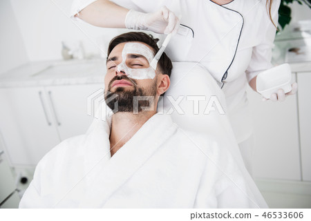 Cosmetologist putting while clay mask on the face of man 46533606