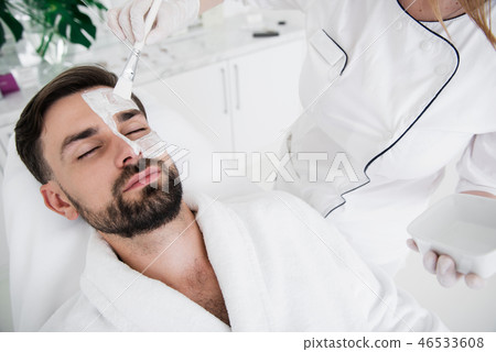 Close up of cosmetologist putting while clay on the face of man Close up of cosmetologist putting while clay on the face of man 46533608