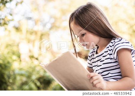 Little girl mindfully reading book in park Little girl mindfully reading book in park 46533942