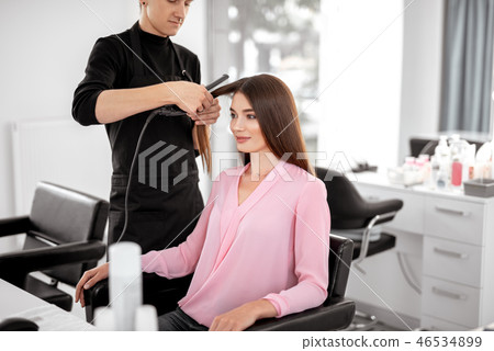 Careful hairdresser using flattening iron and his client smiling Careful hairdresser using flattening iron and his client smiling 46534899