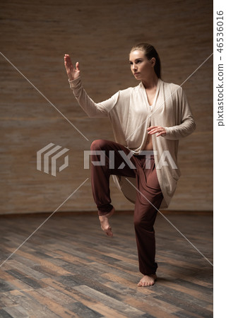 Serious woman putting one leg up while practicing chi gong Serious woman putting one leg up while practicing chi gong 46536016