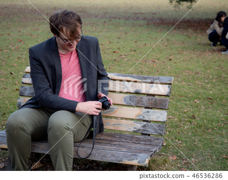 A man sat on a park bench taking pictures 46536286