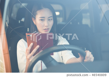 Young Japanese woman driving while looking at a smartphone 46540809