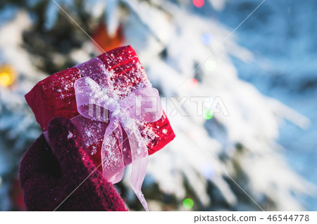 Close-up. Female hand holding red Christmas gift in red mittens in the forest on the background of Close-up. Female hand holding red Christmas gift in red mittens in the forest on the background of 46544778