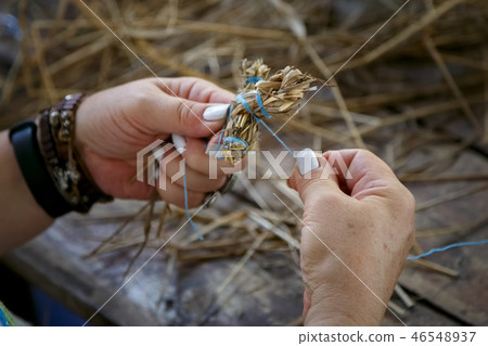 An elderly woman weaves a toy from the straw 46548937