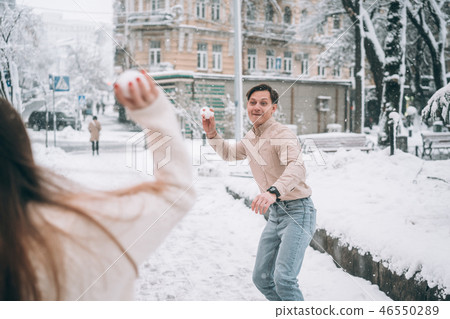 Joyful young couple in sweaters is playing snowballs at the street. Joyful young couple in sweaters is playing snowballs at the street. 46550289