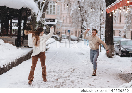 Joyful young couple in sweaters is playing snowballs at the street. 46550290
