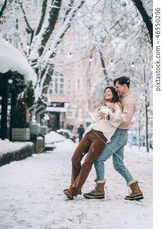 young guy and beautiful girl have fun on a snowy street. Couple in sweaters. young guy and beautiful girl have fun on a snowy street. Couple in sweaters. 46550296