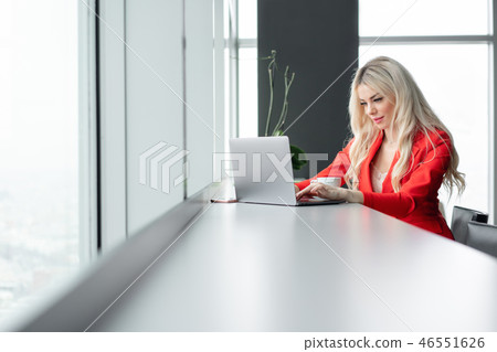Woman in red coral business suit. Young blonde businesswoman with modern gray laptop in the office 46551626