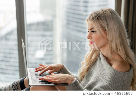 Girl typing on the keyboard. Beautiful blonde woman sitting on the bed and looks at the laptop Girl typing on the keyboard. Beautiful blonde woman sitting on the bed and looks at the laptop 46551693