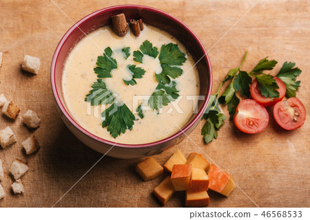 Pumpkin cream soup in bowl with parsley on wooden table with crackers and tomatoes. Traditional Pumpkin cream soup in bowl with parsley on wooden table with crackers and tomatoes. Traditional 46568533