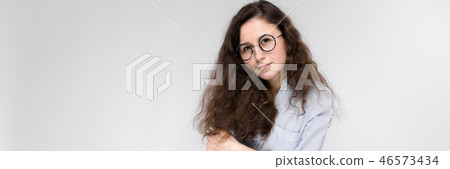 Portrait of a young girl in glasses. Beautiful young girl on a gray background. The girl is holding 46573434