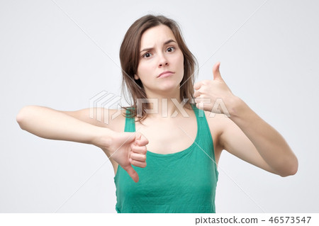 Young woman in green t-shirt showing thumbs up and down sign 46573547