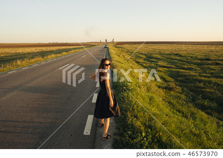 A young girl is walking along the road. She looks around. A young girl is walking along the road. She looks around. 46573970