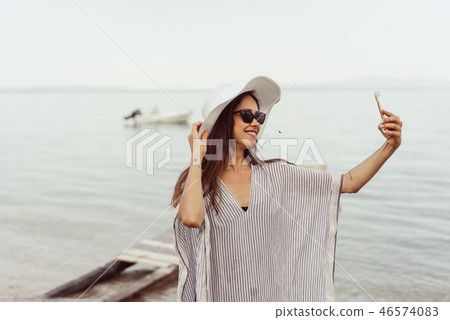 Cheerful young girl in summer hat and swimwear taking a selfie Cheerful young girl in summer hat and swimwear taking a selfie 46574083