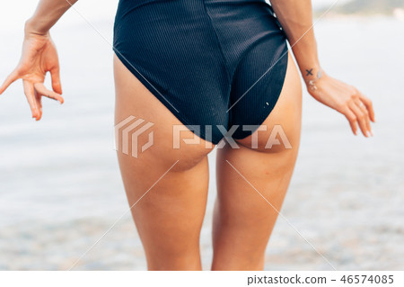 Close-up sexy ass of sporty girl wearing beautiful black swimsuit at the beach. Close-up sexy ass of sporty girl wearing beautiful black swimsuit at the beach. 46574085