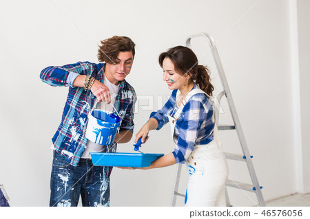People, repair and renovation concept - Beautiful woman and handsome man paints the wall in new 46576056