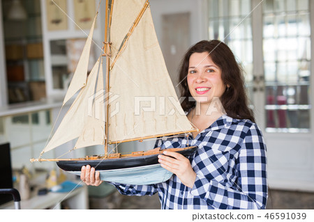 Hobby, interior and collecting concept - young woman holding the layout of a sailboat in the room Hobby, interior and collecting concept - young woman holding the layout of a sailboat in the room 46591039
