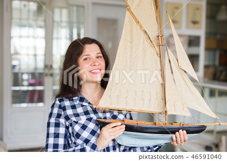Hobby, interior and collecting concept - young woman holding the layout of a sailboat in the room Hobby, interior and collecting concept - young woman holding the layout of a sailboat in the room 46591040
