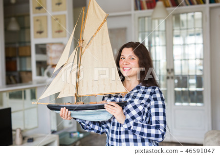 Hobby, collecting, ship and people concept - young woman holding layout of a sailboat 46591047