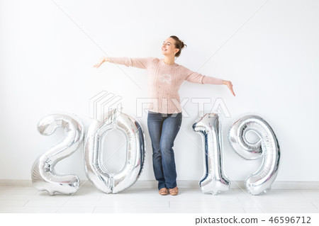 New 2019 Year is coming. Cheerful young woman standing near silver colored numbers in white room 46596712
