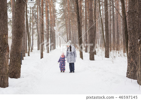 Winter, childhood and people concept - mother is walking with her little daughter in snowy forest 46597145