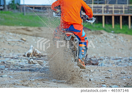 Motorcyclist in a protective suit rides a motorcycle on the sea, splashes fly from under the wheels. 46597146