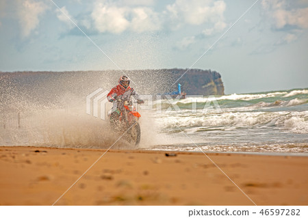 Motorcyclist in a protective suit rides a motorcycle on the sea, splashes fly from under the wheels. Motorcyclist in a protective suit rides a motorcycle on the sea, splashes fly from under the wheels. 46597282