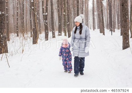 Winter, family and people concept - mother is walking with her daughter in winter forest. 46597924