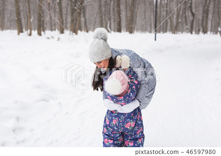 Winter, family and childhood concept - mother is walking with her daughter in snowy forest and 46597980
