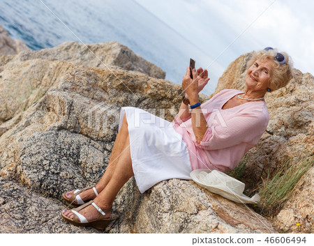 Elderly woman using phone at seaside 46606494