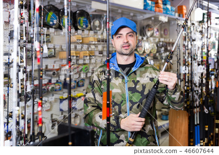 positive fisherman in fishing clothing with fishing rod in the sports shop positive fisherman in fishing clothing with fishing rod in the sports shop 46607644