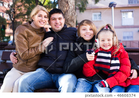 Family sitting on bench outdoors 46608374