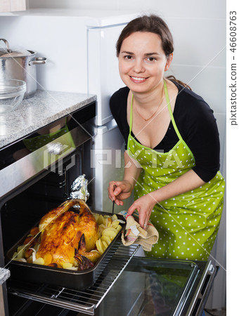 Smiling positive woman roasting cockerel for dinner 46608763