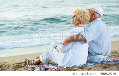 man and woman sitting on the sea shore 46608916