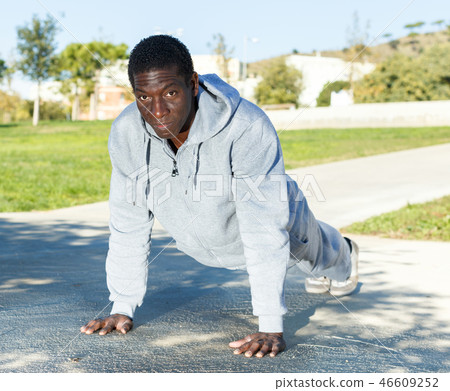 Athletic young male in sportswear training different exercises at park Athletic young male in sportswear training different exercises at park 46609252